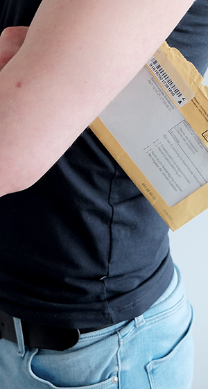 Person hält einen braunen Aktenumschlag, wie er bei einem behördlichen Schreiben verwendet wird, unter dem Arm